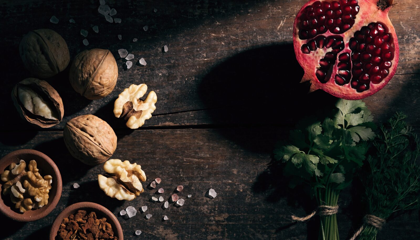 Walnüsse, Granatapfel und frische Kräuter auf dunklem Holz